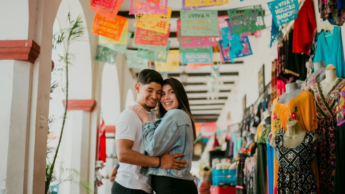 Young couple embracing at a vibrant, traditional Mexican market courtyard.